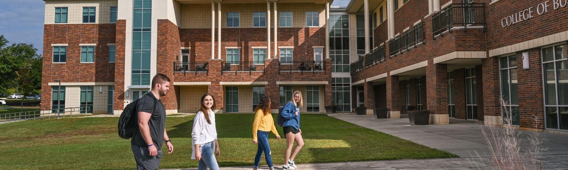 Four College of Business students walk in front of the building