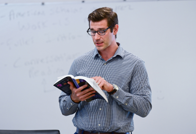 Professor reading from a book in front of a classroom