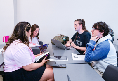 Four students working on laptops and tablets