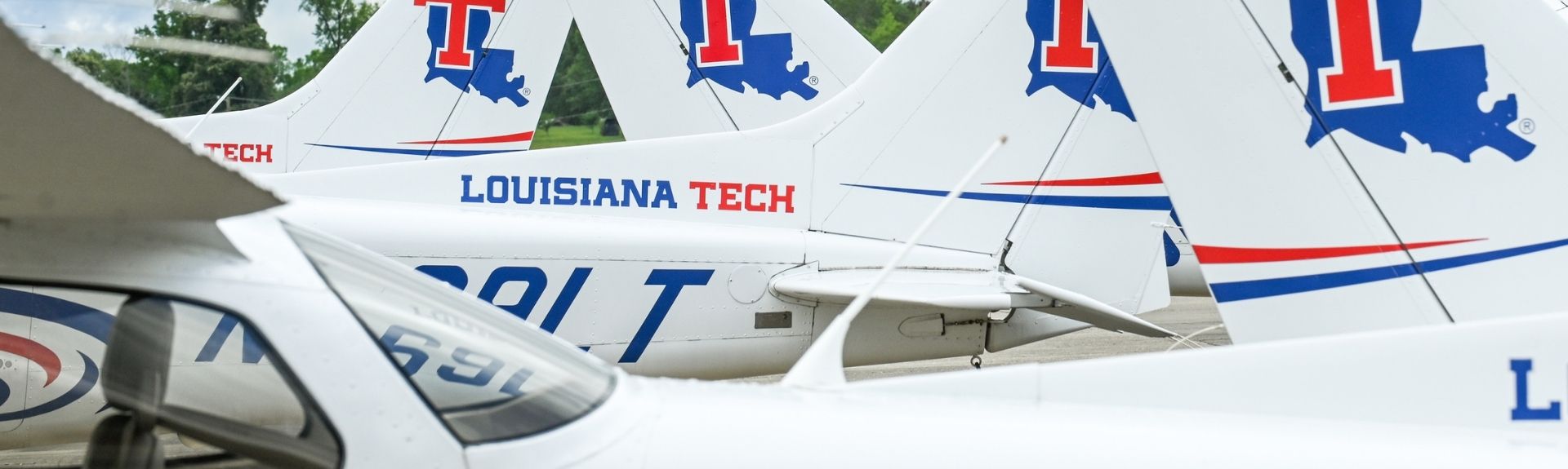 Row of Louisiana Tech University training aircraft parked on the tarmac, showing the tails with the red and blue Louisiana Tech logo