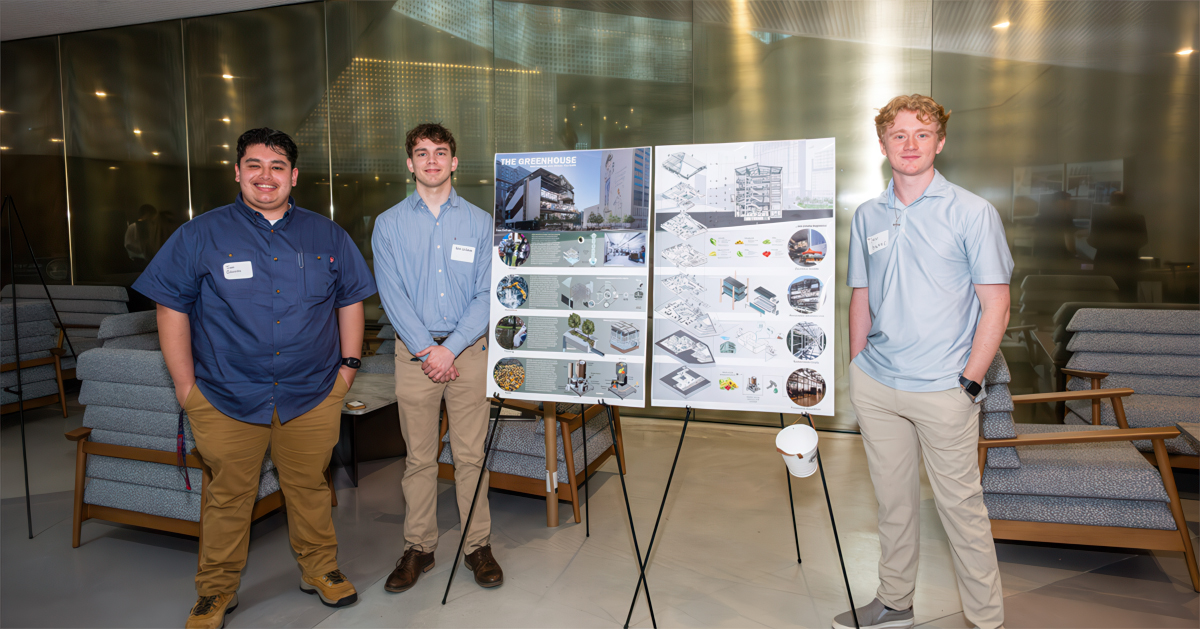 Three architecture students stand near their presentation board
