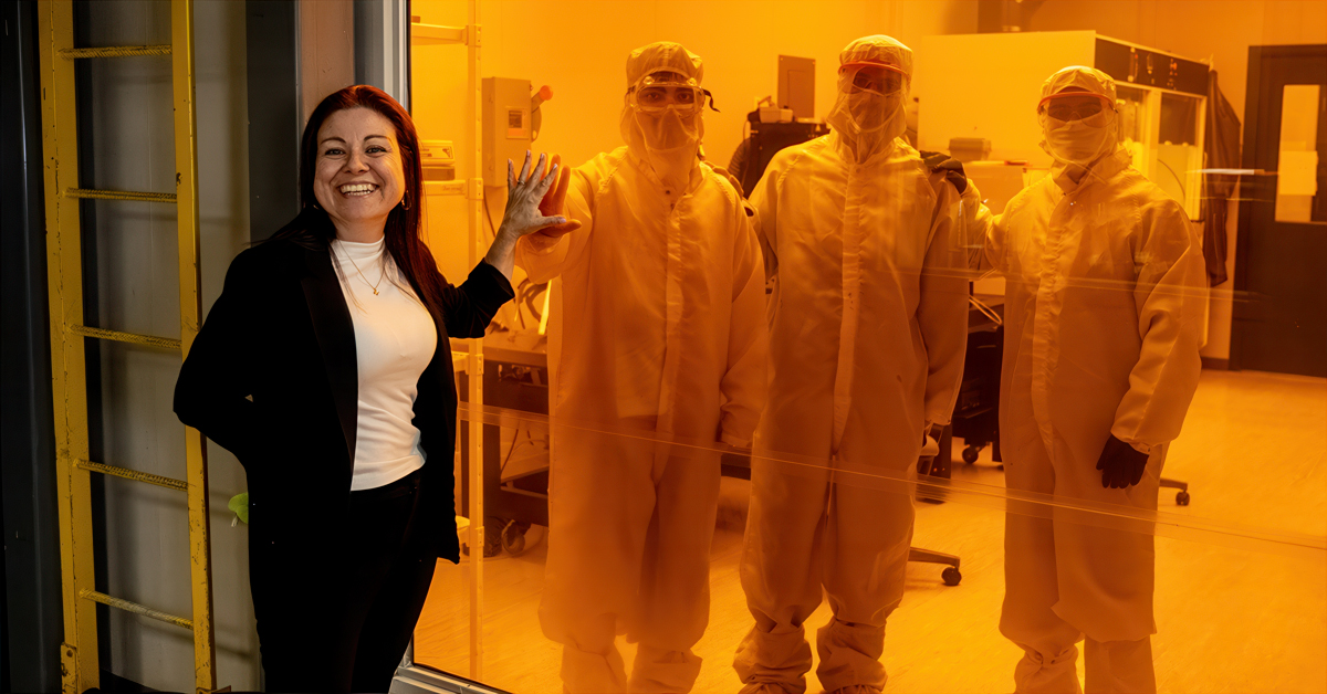 A woman touches hands through glass with researchers in a lab
