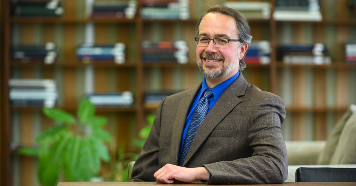 Dr. Kirk St.Amant smiles at a table in a library
