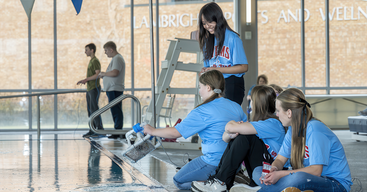 Young students insert a small remote-operated vehicle into an indoor pool