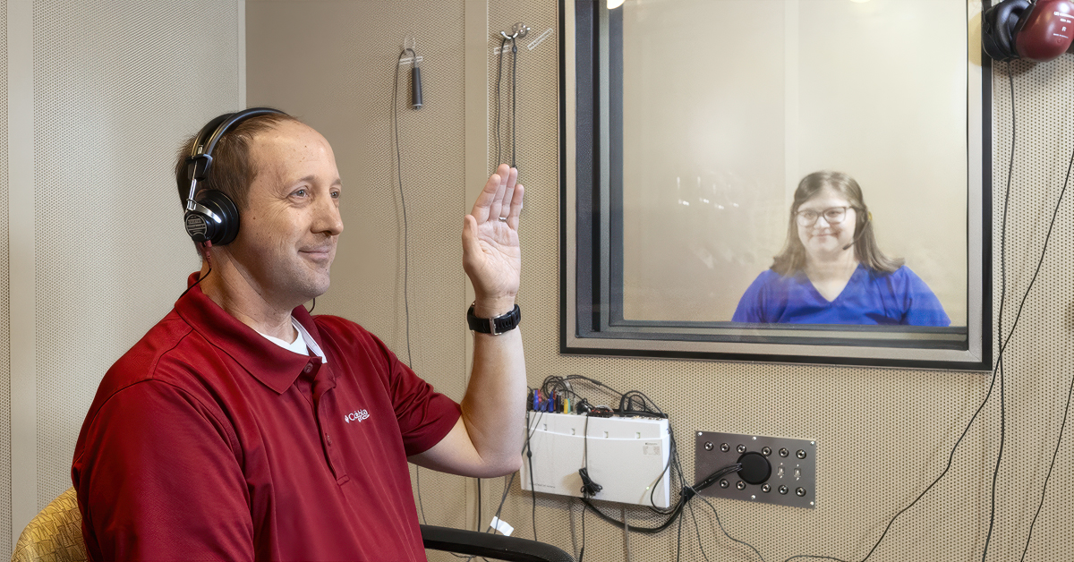A man takes a hearing test while a woman observes through a window