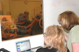 Tech Skilled Nursing Instructors Mary Wilson, left, and Pam Todd control Meti-Man?s health condition behind the new partition and one-way mirror as students go through a medical emergency scenario.