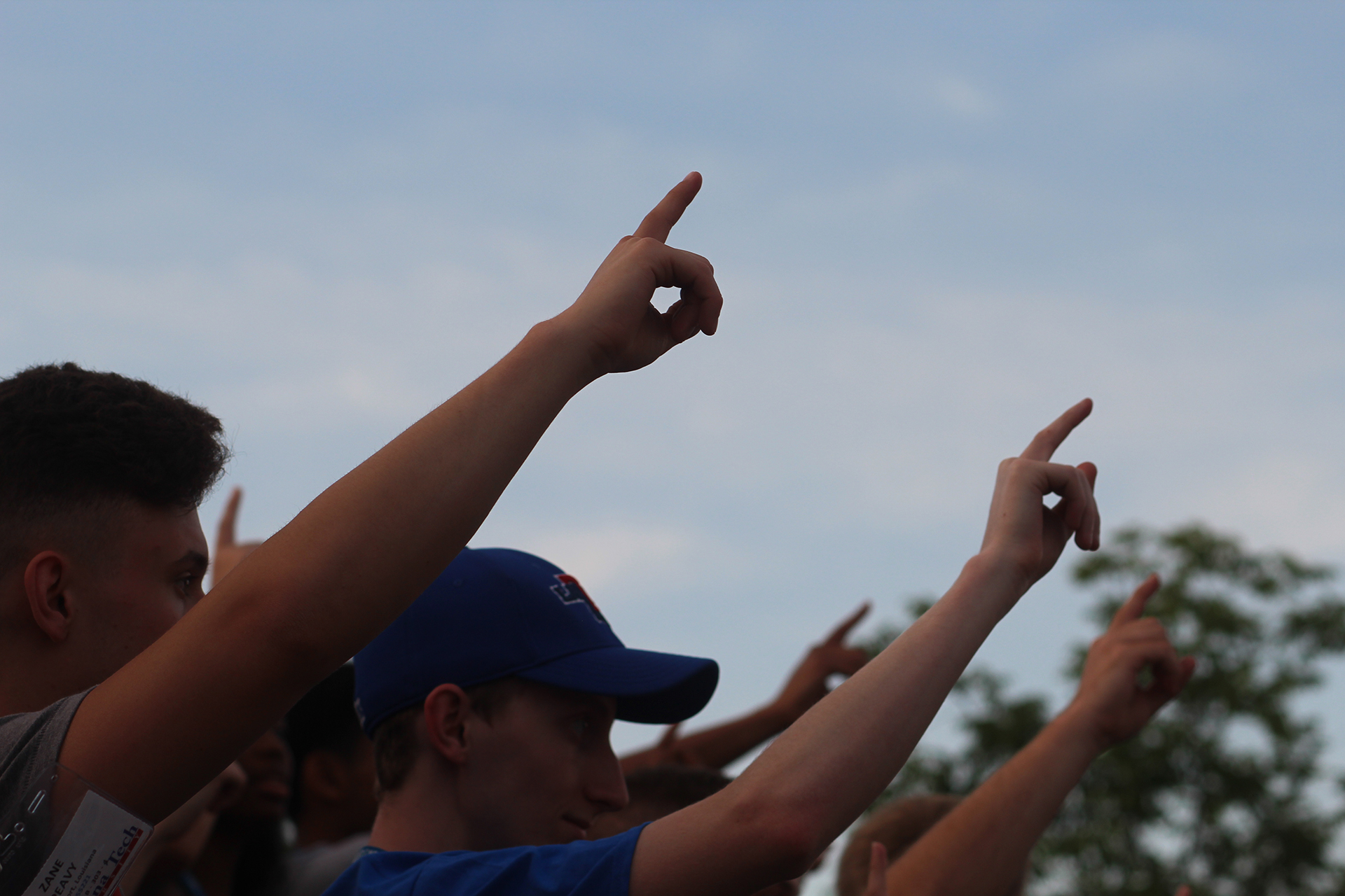 Students holding one finger in the air for Alma Mater
