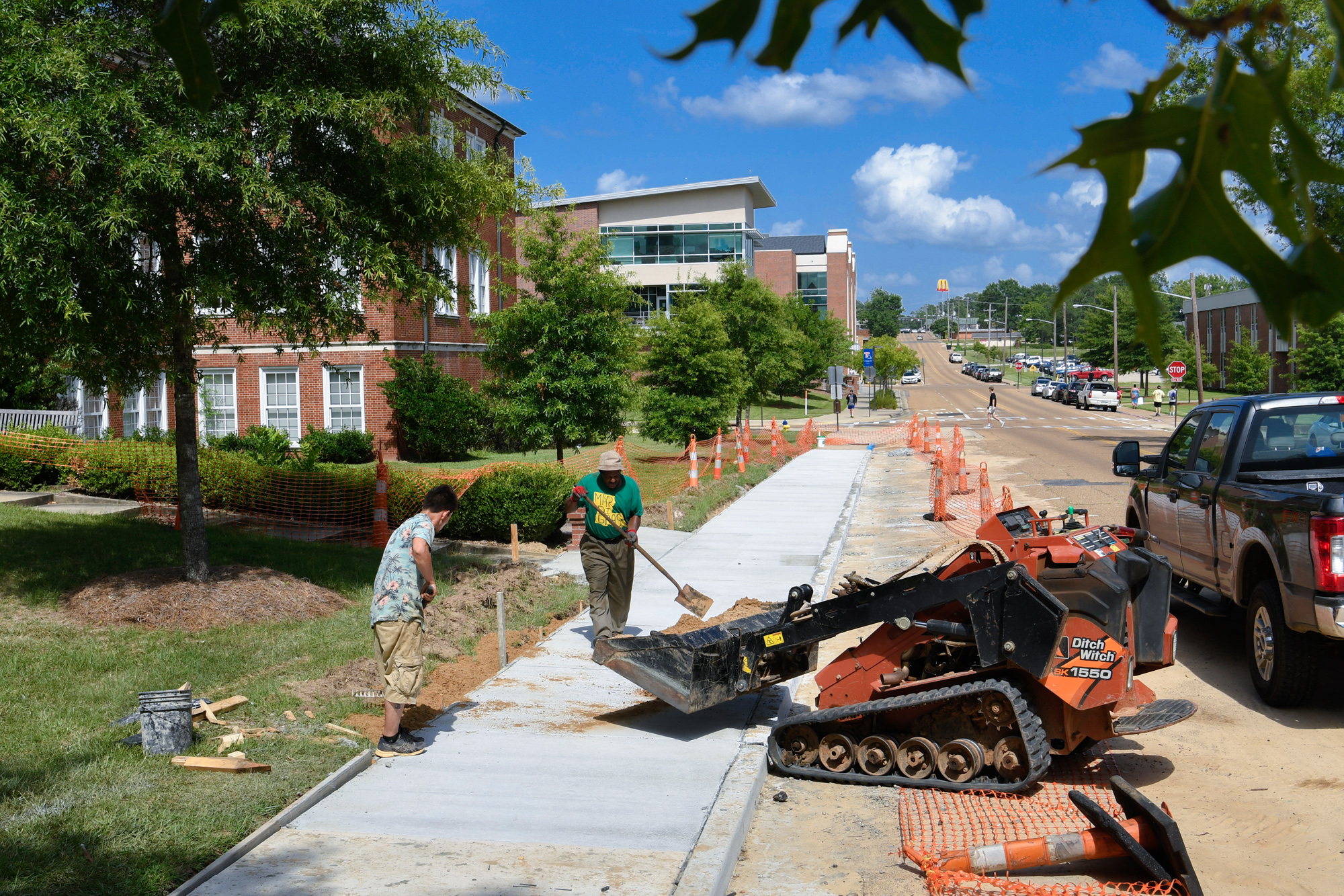 Construction workers shovel dirt to fill in the gaps around newly poured concrete walkways in front of Bogard Hall.