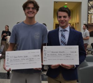 Two male students, Jeremiah Eubanks and John Thomas Butler, stand together with large checks in their hands.